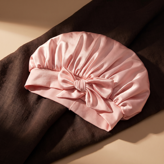 Pink satin sleep bonnet on dark linen, candlelight tones