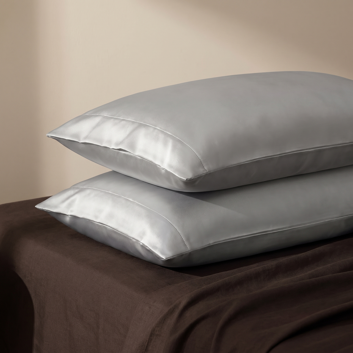 Silver satin pillowcase pair on dark linen bed, warm dusk light