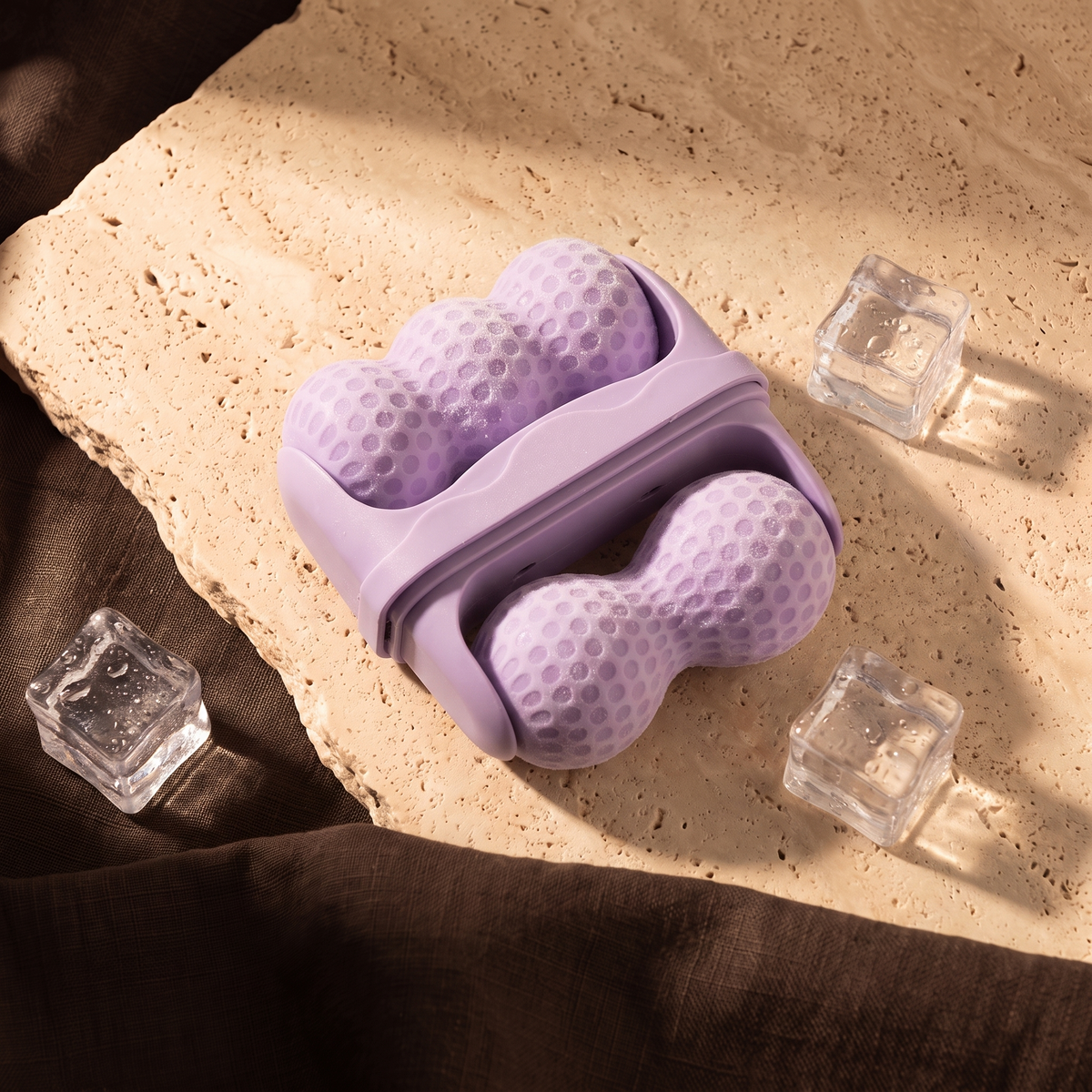 Both rollers uncovered: three-ball roller and curved hourglass roller, on travertine with ice cubes