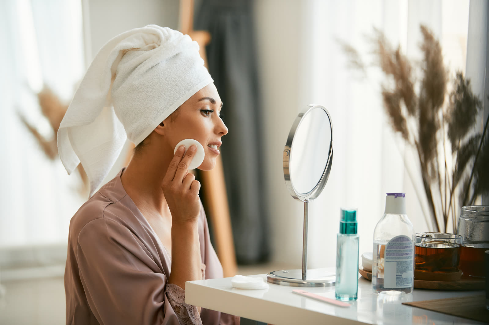 Woman with a towel wrap removing makeup at her vanity in the evening