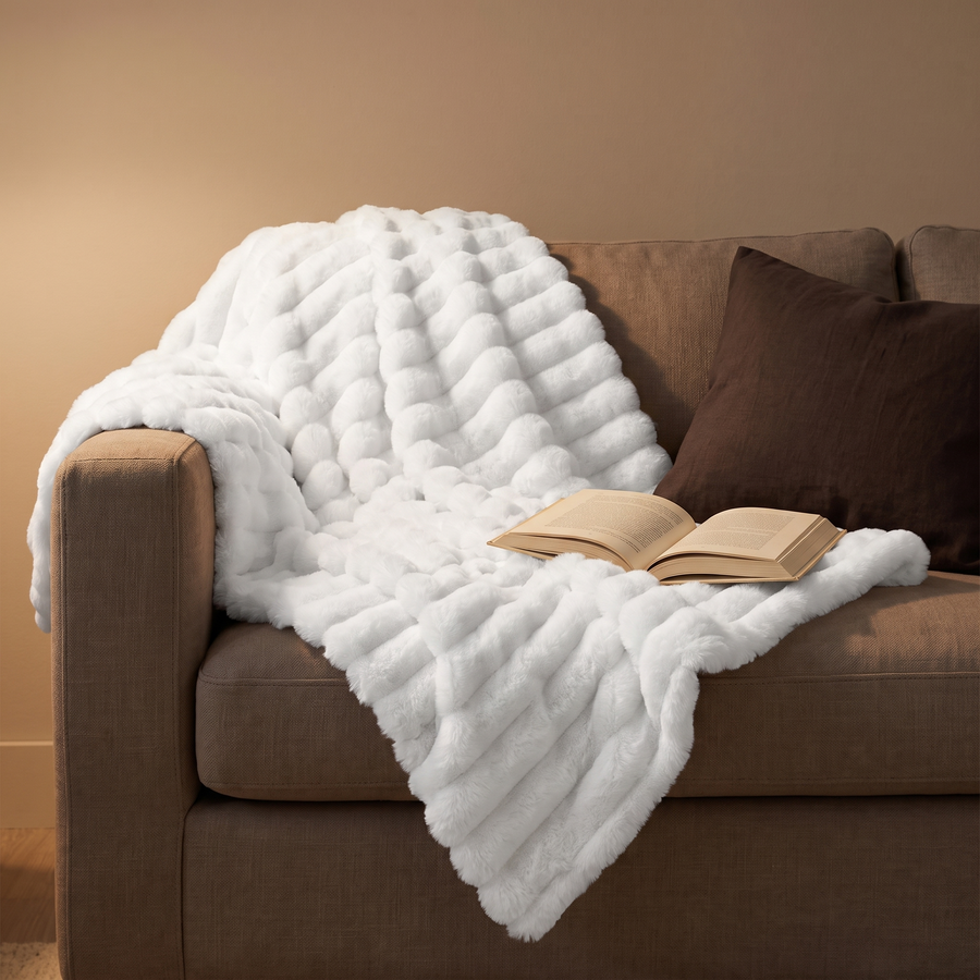 White faux-fur throw draped on a sofa with an open book, evening lamp light