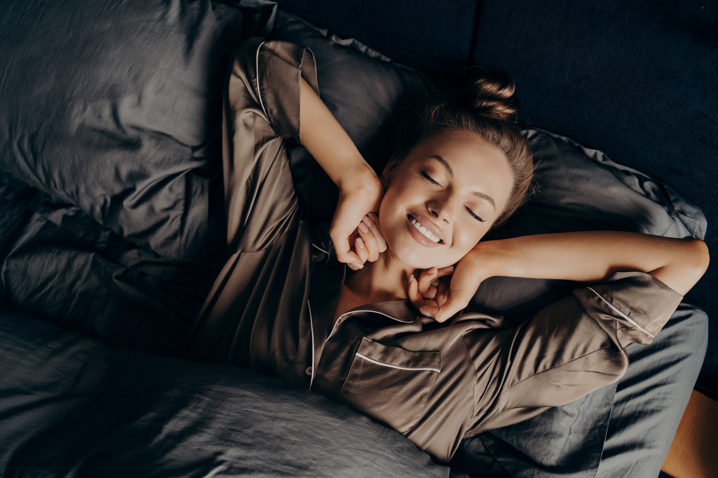 Woman resting her head on a satin pillow, smiling, in warm light